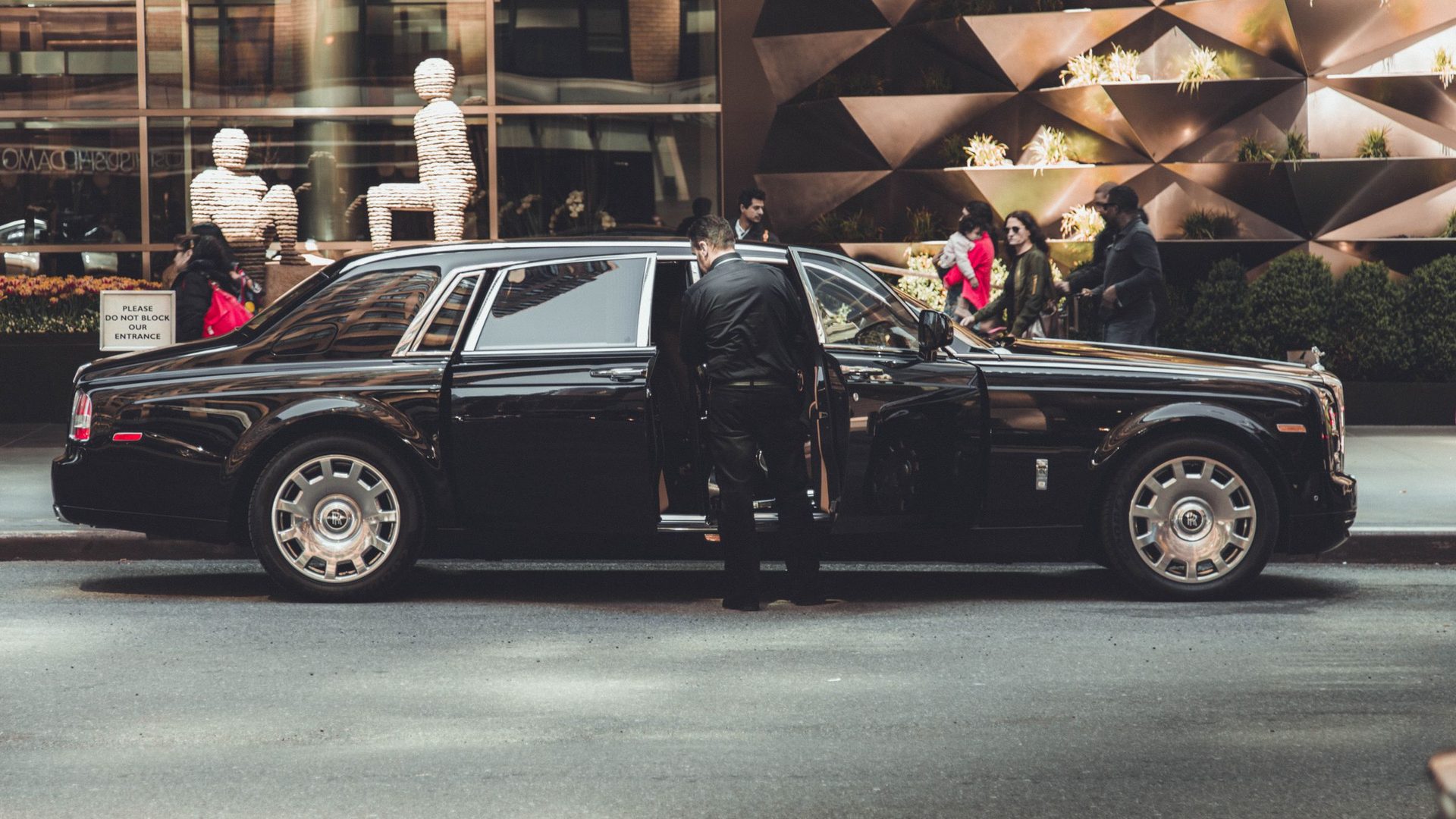 A chauffeur holds the door of a black Rolls-Royce